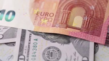 Çelişkili renkler, yazdırılmış işaretler ve kusursuz bir döngü içinde ayrıntılı kağıt dokuları gösteren, avro ve dolar banknotlarının dönüşümlü bir makro görüntüsü..