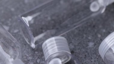 Gri taştan bir yüzey üzerinde duran şeffaflığı, pürüzsüz yüzeyleri ve düzenli yerleştirmeyi vurgulayan şeffaf plastik seyahat şişeleri boyunca yavaş bir pano görüntüsü.