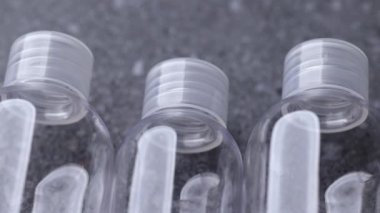 Gri taştan bir yüzeye yerleştirilmiş saydam seyahat şişelerinden oluşan bir yelpazede yavaş bir kamera tepsisi malzeme berraklığını ve basit ürün düzenini vurguluyor..