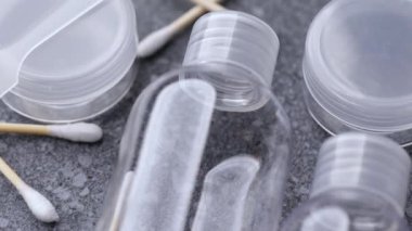 Gri taştan bir yüzeye yerleştirilmiş temiz seyahat şişeleri ve pamuklu çubuklar, hijyen maddeleri, temiz malzemeler ve nötr tasarım vurgulanıyor..