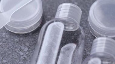 Gri taştan bir zemin üzerinde şeffaf seyahat şişeleri seti, pürüzsüz plastik yüzeyler ve düzenli düzenleme göstermektedir.