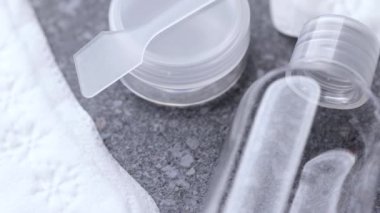 Gri taştan bir yüzeye yerleştirilmiş temiz seyahat şişelerinin yanına yerleştirilmiş kadın pedlerini gösteren bir fotoğraf, hijyen ürünlerini en az düzende sunuyor..