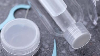 Temiz seyahat şişelerini, gri bir taş yüzeyde diş ipi kürdanlarıyla birleştirerek, hijyen ve kişisel bakım malzemelerini gösteren bir kare..