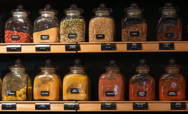 Various colorful spices and herbs displayed in glass jars on wooden shelves for bulk purchase in a retail store