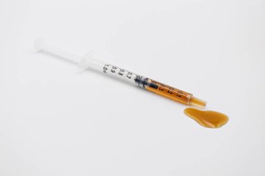 Kalın turuncu-kahverengi sıvı dağıtan şırınga, tıbbi ve esrar kavramlarını vurguluyor