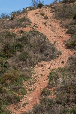 Kirli yol, parlak mavi gökyüzünün altında kurumuş, kayalık araziyi kaplıyor.
