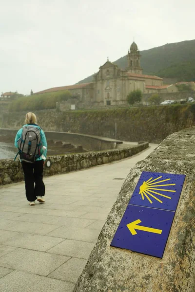 Sırt çantalı kadın yürüyüşçü, sahil yolunda yürüyor, arka planda yön işaretleri ve tarihi mimariyle, keşif ve maceranın özünü yakalıyor. Yüksek kalite fotoğraf