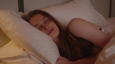 Sakin genç bir kadın, gece rahat bir yatakta mışıl mışıl uyuyor. Kafası yumuşak beyaz bir yastıkta dinlenirken, sıcak bir lambanın altında huzur içinde rüya görüyor..