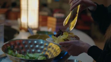 Bir restoranda tabağına taze yeşil marul salatası koymak için maşa kullanan bir kadın sağlıklı ve dengeli bir diyet yaşam tarzını teşvik ediyor..