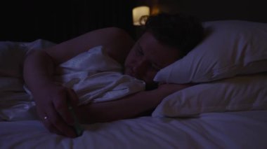 Bilinçsiz bir adam, gece yatağında huzur içinde uyurken dijital detoks ve dinlenme ihtiyacını simgeleyen derin bir uykuya dalarken yanlışlıkla akıllı telefonunu düşürür.