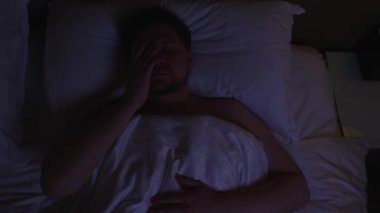 Gece yatakta dönüp duran, stres, endişe ya da uykusuzluk yüzünden uyuyamayan, hayal kırıklığı içinde yüzünü ve gözlerini ovuşturan, uyuyamayan, uykusuzlukla boğuşan bir adam.