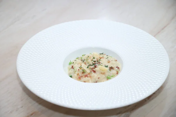 Pirinç, domuz pastırması kırıntıları, parmesan talaşı ve taze otlar ile gurme risotto, beyaz dokulu bir kase üzerinde ustaca düzenlenmiş, güzel bir yemeği ve İtalyan mutfağını sembolize ediyor.