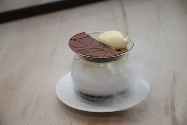 Modern bir tatlıda sunulan vanilyalı dondurma ve çikolatalı garnitür eşsiz bir aşçılık deneyimi için sıvı nitrojenden beyaz bir sis salıyor.