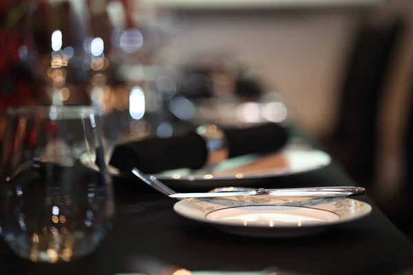 Seramik bir tabak, metal bir bıçak ve su bardağıyla hazırlanmış resmi yemek masası. Restoran ortamında lüks ve sofistike bir ortam sunuyor.
