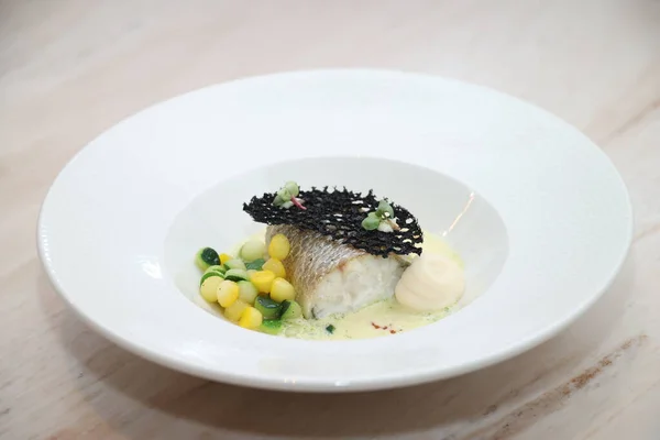 Gurme beyaz balık filetosu renkli sebzelerle, kremalı sosla ve dekoratif çıtır elementlerle süslü, lüks mutfağı ve aşçılık mükemmelliğini temsil ediyor.