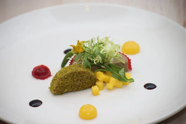 Fıstıkla kaplanmış bir parça yiyecek içeren kaplanmış gurme aperatifi tutarlılık gibi bir ezme, taze yeşil salata, canlı soslar ve doğranmış mango sofistike bir mutfak sunumu yaratıyor.