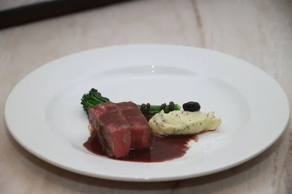 Zengin kırmızı şarap soslu biftek, kremalı patates püresi, taze brokoli ve nefis bir yemek hazırlayan zarif bir garnitür.