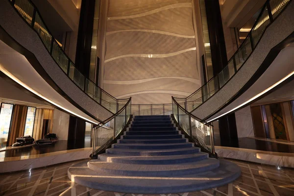 Lüks bir otel lobisinin modern mimarisi mavi halılı ve karmaşık duvar desenli büyük bir merdiven sergiliyor, zarafeti ve üst düzey tasarımı vurguluyor.