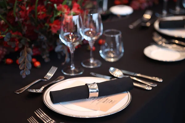 Beyaz tabaklar, siyah peçeteler, parlak çatal bıçak ve temiz şarap kadehleri ile şık bir etkinlik için büyük kırmızı bir çiçek süsü ile ortalanmış zarif resmi yemek masası.