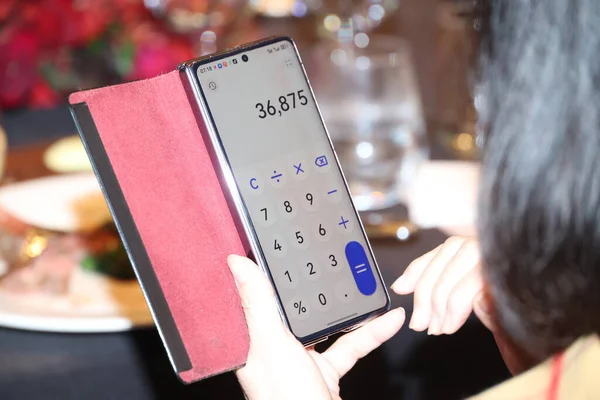 Elinde akıllı telefon tutan, hesap makinesi uygulamasını gösteren, yemek faturasını doğru hesaplayan ve restoran ortamında yemek masraflarını yöneten biri.
