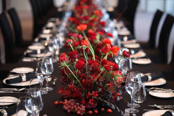 Yer ayarları, gümüş takımlar, cam eşyalar ve sürekli kırmızı çiçekler, üzümler ve küçük böğürtlenlerin yer aldığı bir ziyafet için hazırlanan uzun resmi yemek masası.