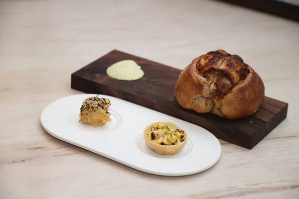 Farklı gurme aperatifler. Ekmek ekmeği, kızarmış kare lokma ve ahşap bir tahtanın üzerinde yeşil soslu mısır tartı. Zarif bir yemek deneyimini temsil ediyor.