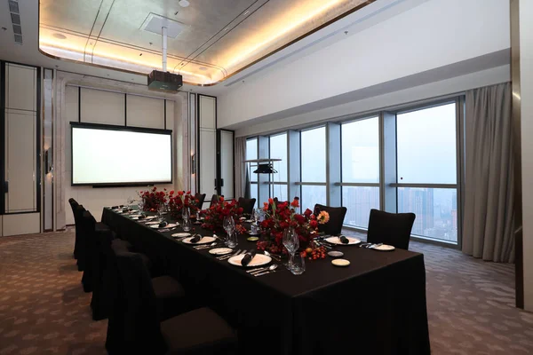 Şatafatlı toplantı odası resmi bir yemek organizasyonu için uzun bir masa seti sunuyor. Zarif çiçek düzenlemeleri, büyük bir projeksiyon ekranı ve panoramik şehir manzarası sunan geniş pencereler.