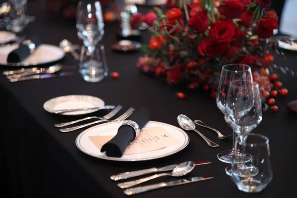 Parlak gümüş takımlı resmi yemek masası, hassas cam eşyalar ve koyu masa örtüsünün üzerinde kırmızı bir gül süsü. Lüks, romantizm ve sofistike kutlama ortamını çağrıştırıyor.