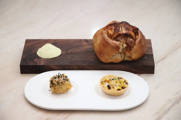 Mısır tartı ve kızarmış deniz tarağı da dahil olmak üzere gurme ekmeği, ahşap bir tabakta pürüzsüz tereyağlı ve rafine bir yemek deneyimi için beyaz tabakta servis edilir.