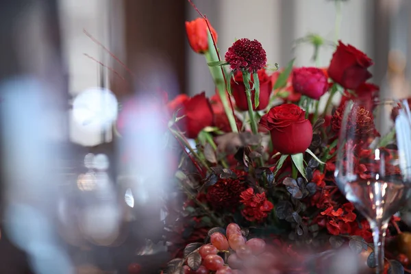 Kırmızı güller, koyu kırmızı çiçekler ve özel durumlar için lüks ve romantik atmosferi çağrıştıran bulanık ön plan bokeh ile zarif yemek masası olarak dizilmiş üzümler.