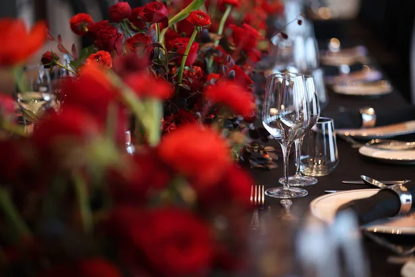 Şatafatlı siyah masa örtüsü, pırıl pırıl cam eşyalar, parlak gümüş eşyalar, taze peçeteler ve canlı kırmızı çiçekli süsler içeren özel bir etkinlik için hazırlanmış şık bir masa.