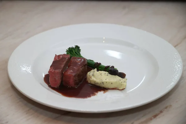 Kırmızı şarap sosuyla kaplı yumuşak biftek dilimleri, yanında kremalı patates püresi ve haşhaş tohumu ve yeşil brokoli, zarif bir gurme yemeği oluşturur.