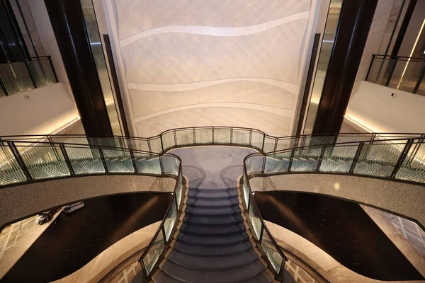 Cam korkuluklar ve yumuşak ışıklandırmalı zarif döner merdivenler büyük bir bina avlusunda lüks ve modern bir iç tasarım yaratarak mimari güzelliği ve modern rahatlığı ön plana çıkarıyor.