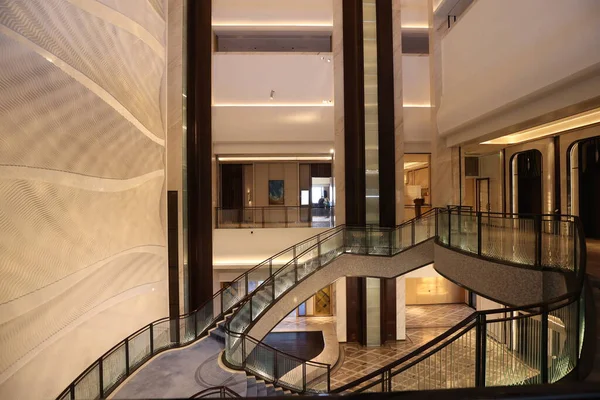 Lüks bir otel lobisine çıkan modern dolambaçlı merdiven. Uzun sütunları, zarif ışıklandırması ve sofistike bir iç tasarım yaratan dalgalı duvar desenleri.