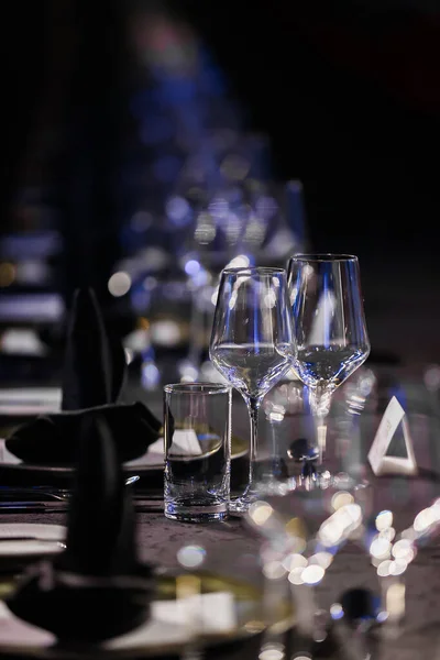 Sofra takımları ve bardak takımları olan lüks sofra takımı resmi bir yemek masasında, yumuşak ortam ışıklandırması özel bir etkinlik için sofistike bir atmosfer yaratıyor.