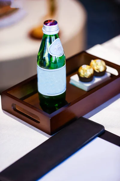 Şişe maden suyu ve premium çikolatalar sofistike, koyu ahşap bir tepsiye konukseverlik, hoş geldin ve lüks konforu temsil eden bir otel odasında veya lüks ortamlarda sunulur.