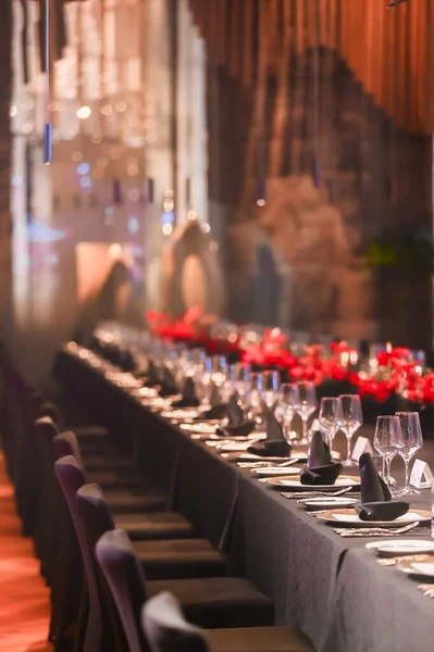 Uzun resmi yemek masası özel etkinlik için hazır, şarap kadehleri, koyu peçeteler, ve sıcak ışık altında canlı kırmızı çiçeklerle süslenmiş yer ayarları