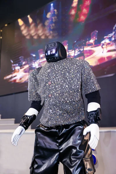 İnsanımsı robot ileri teknoloji ve yapay zeka sergiliyor, fütüristik tarzda giyinmiş, pullu gömlekli ve parlak siyah pantolonlu, aydınlık bir sahnede gösteri yapıyor.