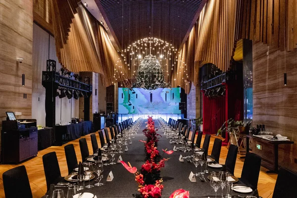 Şık ahşap panelli balo salonunda siyah sofra takımı ve kırmızı anthurium süslemeleri olan uzun bir ziyafet masası. Zarif bir gala resepsiyonu için ortam ışıkları ve avizeler.