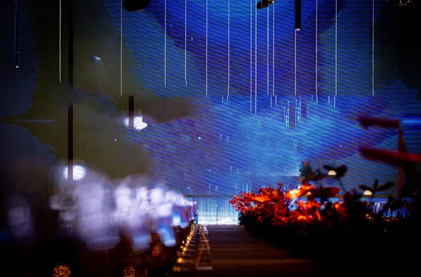 Soyut mavi ışık ince desenli bir duvar boyunca uzanırken sıcak kırmızı ve turuncu ışıklar ön plandaki bulanık elementleri aydınlatarak fütüristik, karanlık bir atmosfer yaratıyor.