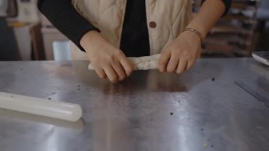 Kadın fırıncı, profesyonel mutfakta paslanmaz çelik tezgahta ustalıkla hamur yoğurup yuvarlayarak ekmek ya da hamur işi pişirmek için malzemeler hazırlar.