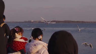 İki küçük çocuğun su kenarında oturup, güzel ve sakin bir günbatımında zarif bir şekilde uçan ve yiyecek yakalayan büyük bir martı sürüsünü izlediğini ve beslediğini düşünün.