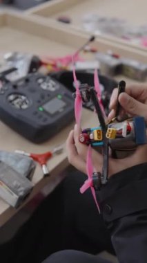 Becerikli eller, bataryayı özel yapım bir fpv insansız hava aracına bağlarken kuadkopteri uzaktan kumandalı ve arka plandaki tezgahta hazır olan bir gözlükle uçuşa hazırlıyor.