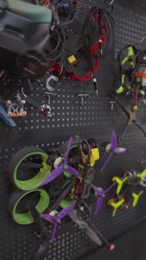 Atölyedeki siyah tahta duvarda asılı renkli özel yapım birinci şahıs yarışı ve serbest stil dronlar var. Amatör kuadkopter koleksiyonu ve yarış fpv dronları sergileniyor.