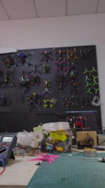 Fpv insansız hava aracı atölyesindeki çalışma tezgahının ayrıntılı görüntüsü, inşa araçları, fpv insansız hava araçlarının onarımı, askeri kullanıma adapte edilmiş ticari elektronik cihazlar, arka planda asılı çeşitli fps kuadkopterleri