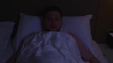 Korkmuş genç bir adam, kabustan ve evdeki karanlık odasında uykusuzluktan korkarak ve endişeli bir şekilde gece yatağında uykusuzluktan uyanıyor.