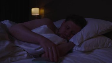 Sinirli adam sabah akıllı telefonunun alarmını kapatıyor, uyanmaya hazırlanıyor ve yeni bir güne başlıyor, ama sıcak örtülerin altında rahat yatağında uyumaya devam etmek istiyor.