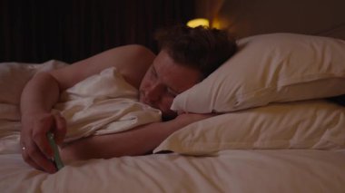 Genç beyaz bir adam gece rahat bir yatakta uyuyakalıyor. Akıllı telefonunun elinden kayıp gitmesine izin veriyor. Teknoloji bağımlılığını, yorgunluğu ve dijital detoks ihtiyacını simgeliyor.