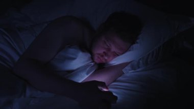 Telefon bağımlılığı olan uykusuz bir adam sosyal medyada ya da internet haberlerinde dolaşmak yerine geceleri uyuyan yüzü karanlık yatak odasındaki parlak ekran ışığıyla aydınlatılıyor.