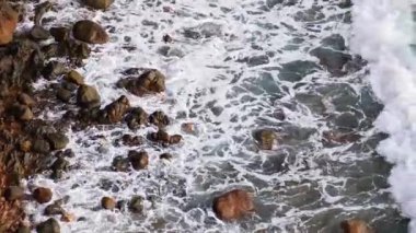Yavaş çekimde okyanus dalgaları kayalık kayalıklara çarpıyor ve ritmik hareketlerle püskürtüyor. Doğa, kıyı, deniz ve manzaralı arka plan kullanımı için ideal.